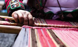 An indigenous person weaving colorful fabric.